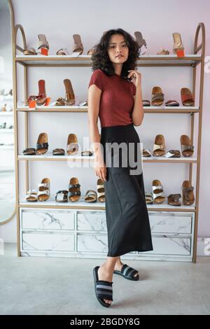 asiatische Frau posiert vor Schuhregalen im Boutique-Shopping-Shop Stockfoto