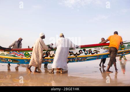 Die Crew-Mitglieder von Mohammed Sovv's Fischfang Pirogue schleppen ihr Boot nach einem Tag lang vor der Küste von Nouakchott, Mauretanien. Stockfoto