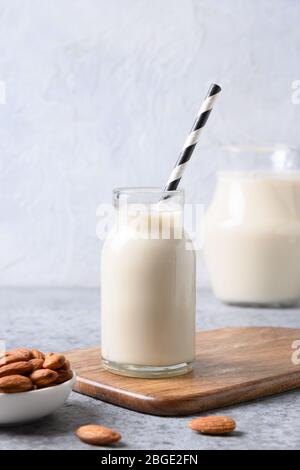 Frische Mandelmilch in Glasflasche und Nüsse auf grauem Hintergrund. Nahaufnahme. Gesunde vegane Ernährung. Mangel an Cholesterin. Stockfoto