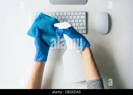 Nahaufnahme der Hände in Handschuhen mit Desinfektionsmittel und einem Lappen für die Verarbeitung eines Büroarbeitsplatzes. Stockfoto