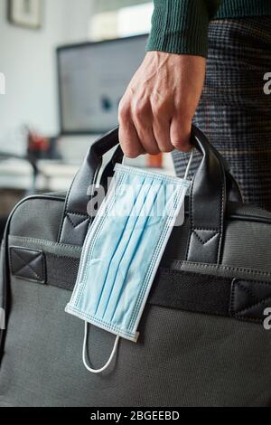 Nahaufnahme eines jungen Mannes in einem Büro, der eine Aktentasche und eine OP-Maske in der Hand hält Stockfoto