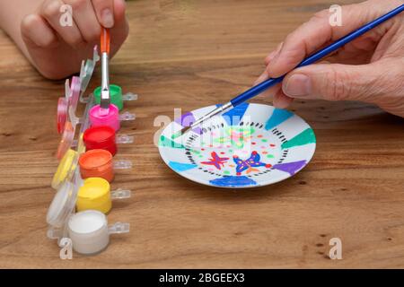 Erwachsene und Kinder Hände malen ein Porzellan Schüssel mit einem Pinsel und einem Satz Farbe in verschiedenen Farben in einem Holztisch. Hobby-Konzept Stockfoto