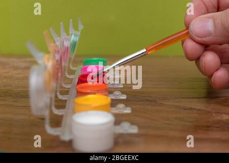 Erwachsene Hände tauchen einen Pinsel in Acryl-Farbtöpfe in verschiedenen Farben auf einem Holztisch. Hobby-Konzept Stockfoto