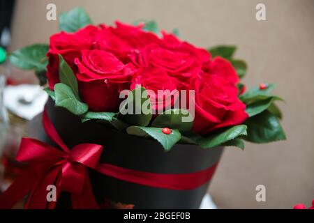 Ein Strauß von roten und weißen Rosen in einer roten runden Box.Blumenstrauß aus roten Rosen, dunkelroten Nelken, schwarzen Beeren und grünen Blättern in die gesetzt Stockfoto