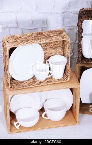 Schöne Regale und Boxen mit Geschirr auf hellen Wand Hintergrund Stockfoto