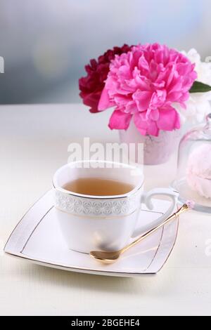 Zusammensetzung der wunderschöne Pfingstrosen in Vase, Tee in Tasse und Marshmallow, am Tisch, auf hellen Hintergrund Stockfoto