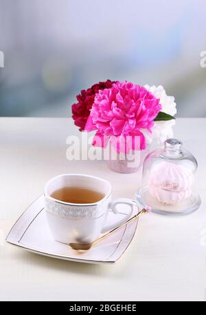 Zusammensetzung der wunderschöne Pfingstrosen in Vase, Tee in Tasse und Marshmallow, am Tisch, auf hellen Hintergrund Stockfoto
