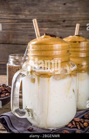 Trendiges Getränk, Dalgona Kaffee. Peitschte Instant-Kaffee-Getränk mit kalter Milch und Zucker. Flauschig cremig Schlagsahne Kaffee Getränk, auf Holz rustikalen backgroun Stockfoto