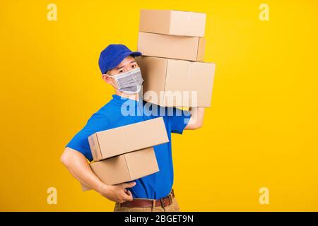 Asiatische junge Lieferarbeiter Mann in blauen T-Shirt und Mütze Uniform tragen Gesichtsmaske Schutz Heben Stapel eine Menge Boxen, unter Coronavirus oder COVID- Stockfoto