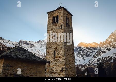 Alte mittelalterliche Glockenturm einer alten Steinkirche in der Nähe des Bergmassivs des Monte Rosa (Piemont, Italien), im Licht des Sonnenuntergangs Stockfoto