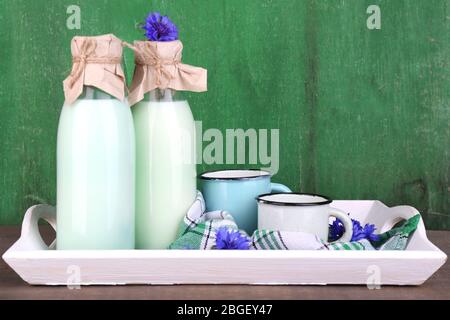 Flaschen und Tassen Milch mit Kornblumen auf Holztablett Stockfoto