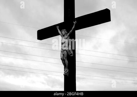 Kruzifix mit vergoldeter Skulptur Jesu auf Holzkreuz gegen dunklen Himmel. Stockfoto