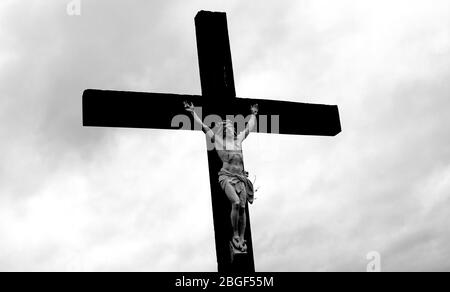 Kruzifix mit vergoldeter Skulptur Jesu auf Holzkreuz gegen dunklen Himmel. Stockfoto