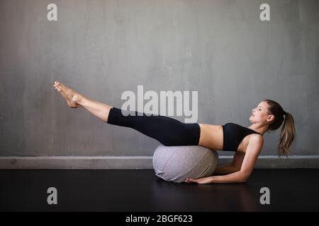 Eine kaukasische Frau Pilates Fitness trainieren schweizer Ball Übungen isoliert auf industriellen Hintergrund, moderne Wohnung Stockfoto