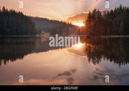 Wunderschöner Blick auf den Sonnenuntergang mit Sonnenstrahlen über einem Bergsee. Shiroka Polyana Damm in Rhodopi Gebirge, Bulgarien. Stockfoto