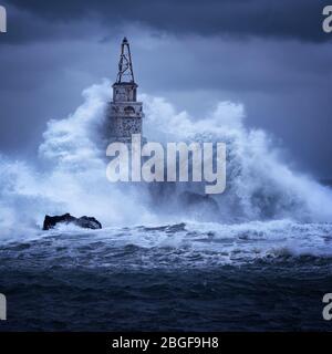 Große Welle gegen den alten Leuchtturm im Hafen von Ahtopol, Schwarzes Meer, Bulgarien an einem stürmischen Tag. Gefahr, dramatische Szene. Stockfoto