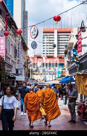 Singapur, 2019. Oktober: Buddhistische Mönche in orangefarbenen Roben gehen an einem sonnigen Tag eine belebte Straße in Singapurs Chinatown entlang Stockfoto