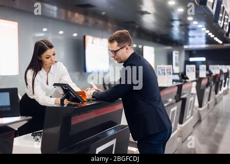 Business Reise. Hübscher junger Geschäftsmann in Anzug Holding seinen Pass und im Gespräch mit Frau am Check-in-Schalter im Flughafen Stockfoto