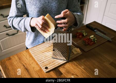 Ein junges Mädchen bereitet Essen, Reibenkäse, in einer Küche zu Hause mit Zutaten auf einer Arbeitsfläche. Stockfoto