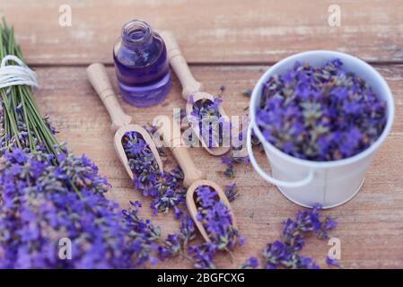 Draufsicht auf eine Schüssel und Holzlöffel mit frischen Lavendelblüten, ätherischem Lavendelöl und einem Bouquet von Lavendel auf einem braunen Holzhintergrund. Stockfoto