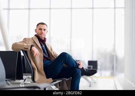 Der junge Geschäftsmann wartet in der Wartehalle des Flughafens und er überprüft die Zeit auf seiner Uhr. Stockfoto