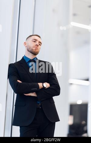 Mann mittleren Alters stehend mit gefalteten Armen an einer Fensterbank gelehnt Drehen, um die Kamera mit einem nachdenklichen Ausdruck zu betrachten Stockfoto