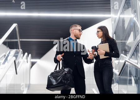 Ein Geschäftspaar auf einer Treppe, das sich unterhielt und lächelte. Mann in Anzug und Brille mit Tasche und Gespräch mit einer Frau, die einen Tablet-Computer hält. Stockfoto
