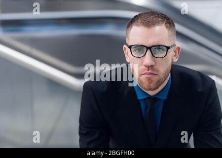 Eleganter junger erwachsener Mann auf der Treppe mit Tasche in der Hand. Er schaut zur Seite. Stockfoto