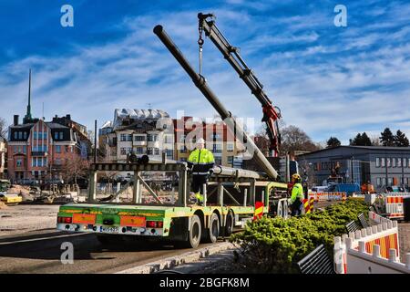 Männer, die mit einem LKW-Kran arbeiten, um die Rohre auf der Straße in Helsinki, Finnland zu entladen. 25. März 2020. Stockfoto