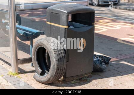 Nahaufnahme eines Autoreifens und schwarzer Taschen, die neben einem öffentlichen Müllbehälter stehen Stockfoto