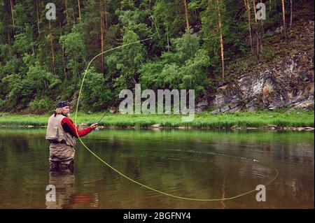 Fliegenfischen Angler macht werfen, während im Wasser stehen Stockfoto