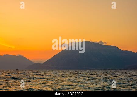 Küste und hohe Berge bei Sonnenuntergang. Zwei Windparks und eine Wolke auf der Spitze Stockfoto