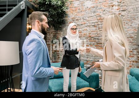Ziemlich muslimische arabische Geschäftsfrau in weißen Hijab Händeschütteln mit ihren kaukasischen Partnern oder Kunden beim Treffen von Mann und Frau am Arbeitsplatz in Stockfoto