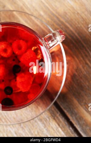 Fruchtroter Tee mit Waldbeeren in Glasbecher, auf Holzhintergrund Stockfoto