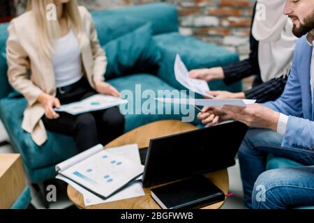 Bild für Business Meeting zugeschnitten. Junge multiethnische Menschen arbeiten im Büro, sitzen auf dem Sofa um den Holztisch mit Laptop, Notebook und Stockfoto