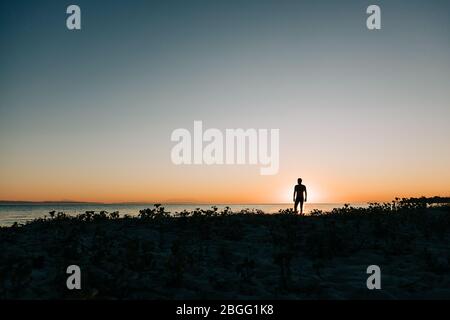 Silhouette eines Mannes, der den Sonnenuntergang am Strand genießt Stockfoto