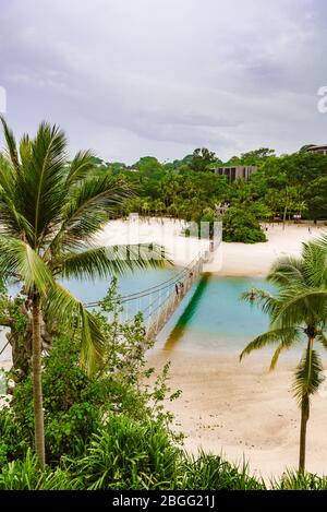 Blick von oben auf die schwimmende Brücke am Siloso Beach, Palawan Beach auf Sentosa Island, Singapur. Hängebrücke in tropischem Klima mit Palmen Stockfoto