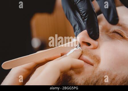 Haarentfernung mit Wachs aus der Nase des Mannes, Schönheits- und Pflegeverfahren Depilation im Barbershop Stockfoto