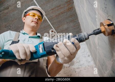 Bauarbeiter pneumatische Hammerbohrer Bohrung in Betonziegelwand mit Rautenkrone für Elektrokabel, Steckdose, Schalter Stockfoto