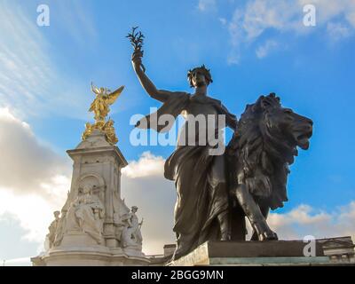 Statue einer Frau und eines Löwen mit dem Hauptteil des Victoria Memorial im Hintergrund, direkt vor dem Buckingham Palace, in London, Großbritannien Stockfoto