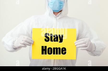 Stay Home Text auf gelben Warnschild in Ärzte Hände in Schutzanzug Gefahr und Gesicht chirurgische Maske. Coronavirus, Covid-19-Selbstquarantäne Stockfoto