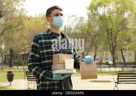 Kurier in Schutzmaske und medizinischen Handschuhen liefert Essen zum Mitnehmen Stockfoto