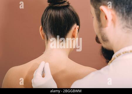 Akupunkturnadeln in der Wirbelsäule einer Frau Nahaufnahme auf einem braunen Hintergrund. Reflexologe sehr genau tun Akupunktur. Osteochondrose-Behandlung Stockfoto