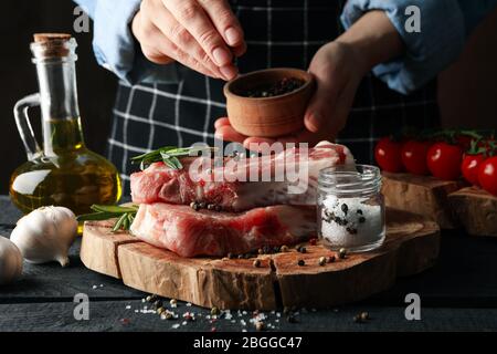 Person streut Gewürze auf rohes Fleisch. Konzept für das Kochen von Steak Stockfoto