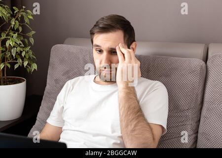 Stress kaukasischen düsteren Mann im Stress arbeitet aus dem Home Office mit Laptop und Internet. Telearbeit, Freiberufler, Arbeitsplatz im Home Office auf dem Sofa Stockfoto