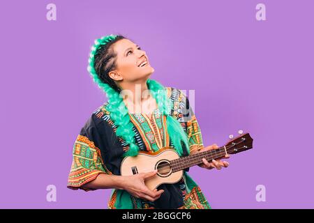 Schöne Frau mit Kanekalon Zöpfe spielen Ukulele. Stilvolle Frisur Kanekalon Zöpfe. Hawaiianische Gitarre auf violettem Hintergrund Stockfoto