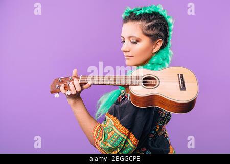 Rastafari Frau mit Ukulele auf der Schulter. Musikinstrument Ukulele. Hawaiianische Gitarre auf violettem Hintergrund Stockfoto