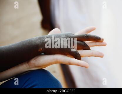 Schönes Bild von Menschenrechtsfragen: Weiße Frau und schwarzes Kind halten die Hände in einem Zeichen der Liebe. Stockfoto