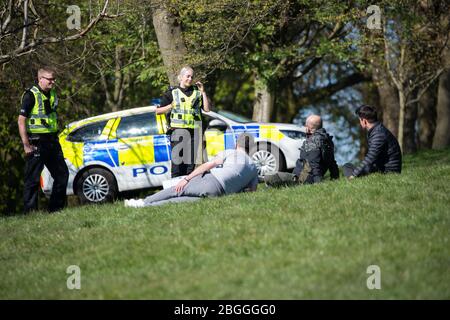 Glasgow, Großbritannien. April 2020. Im Bild: Eine Polizeiwache spricht mit Menschen, die auf dem Gras liegen und sich sonnen und sie weiterbewegen, während sie die Coronavirus-Gesetzgebung von einer Stunde Bewegung pro Tag durchsetzen. Szenen aus dem Kelvingrove Park in Glasgow während der Sperrung des Coronavirus (COVID-19). Quelle: Colin Fisher/Alamy Live News Stockfoto