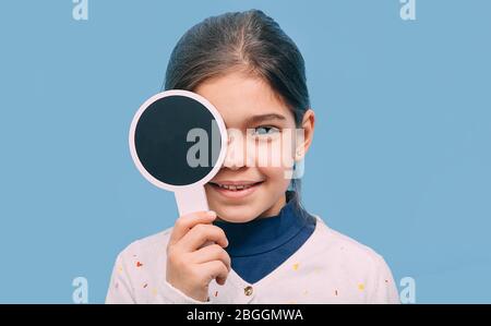 Lächelndes Mädchen, das die Augen überprüft und die Augen mit einem speziellen Werkzeug auf blauem Hintergrund schließt. Vision Test Konzept Stockfoto